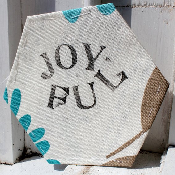 A fabric hexagon with "joyful" stamped on in black ink.