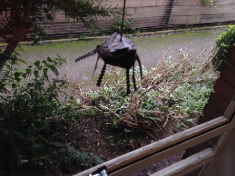 A spider made from egg box and bicycle inner tube dangles in front of a window