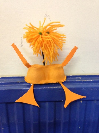 A bright orange alien made of egg boxes, and a wool pompom for a head sits on the radiator. 